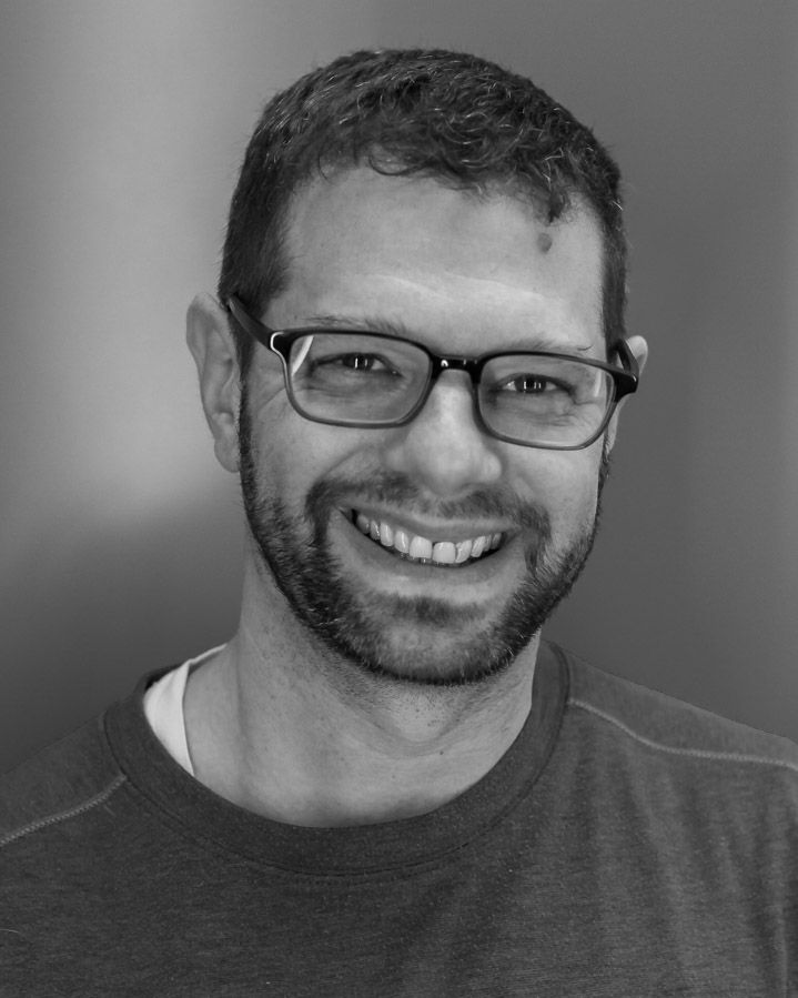 Black-and-white portrait of David, the Muttographer photographer, smiling and wearing glasses.